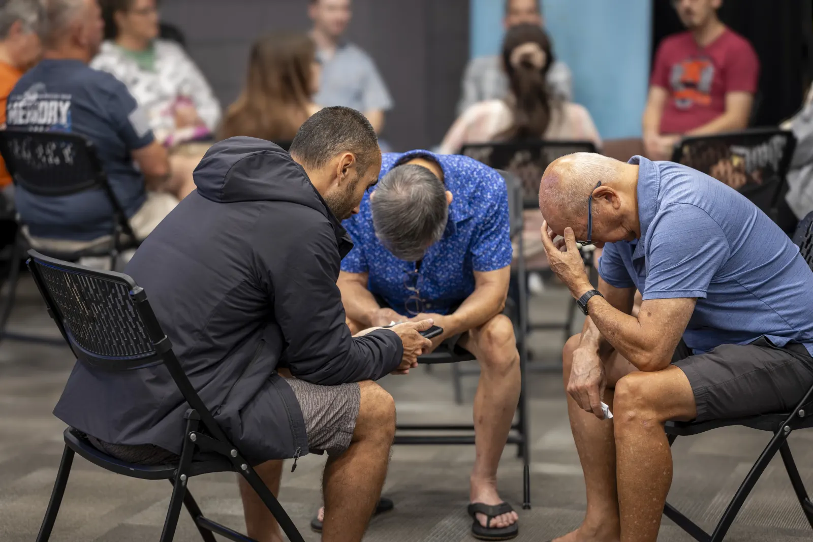 Three men in a small group circle, heads bowed in prayer