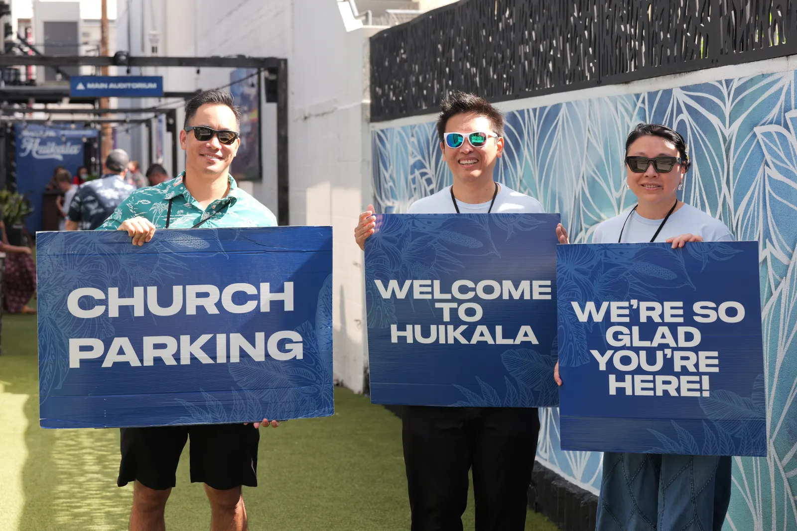 Huikala greeters holding signs that read Church Parking, Welcome to Huikala, and We're so glad you're here!